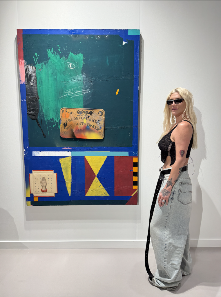 Pop star Ke$ha stands in front of a painting. 